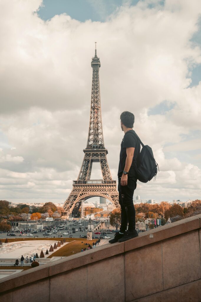 A tourist stands with a backpack admiring the Eiffel Tower in Paris during the day.
