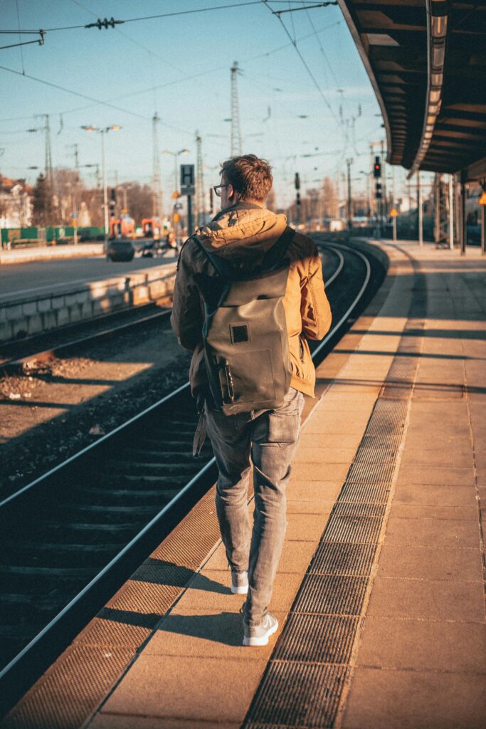 A man with a backpack walks along a train platform, capturing a journey moment in urban daylight.