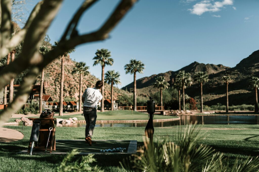 Golfer practicing swing with scenic mountain and palm tree backdrop, outdoors.