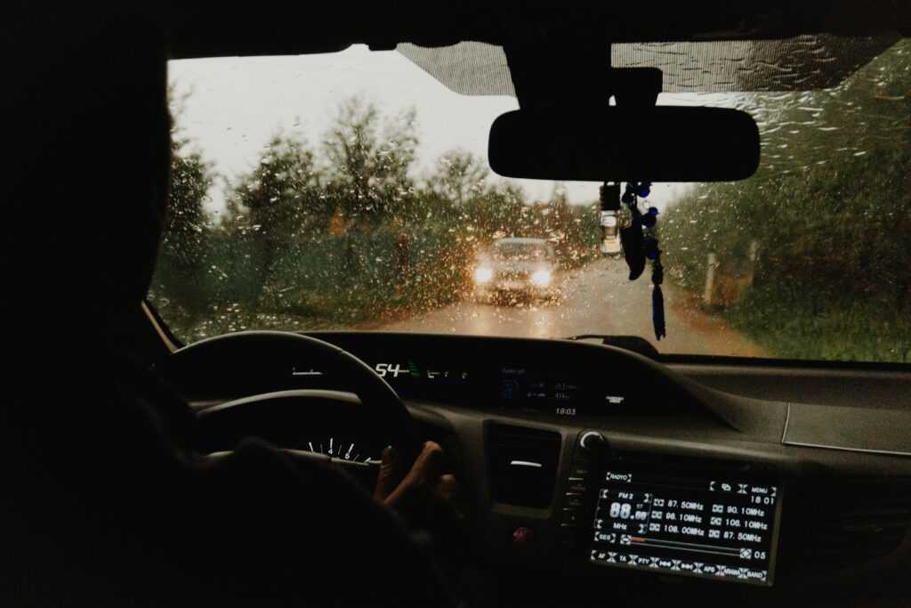 Interior view of a car driving through a rural road in the rain.